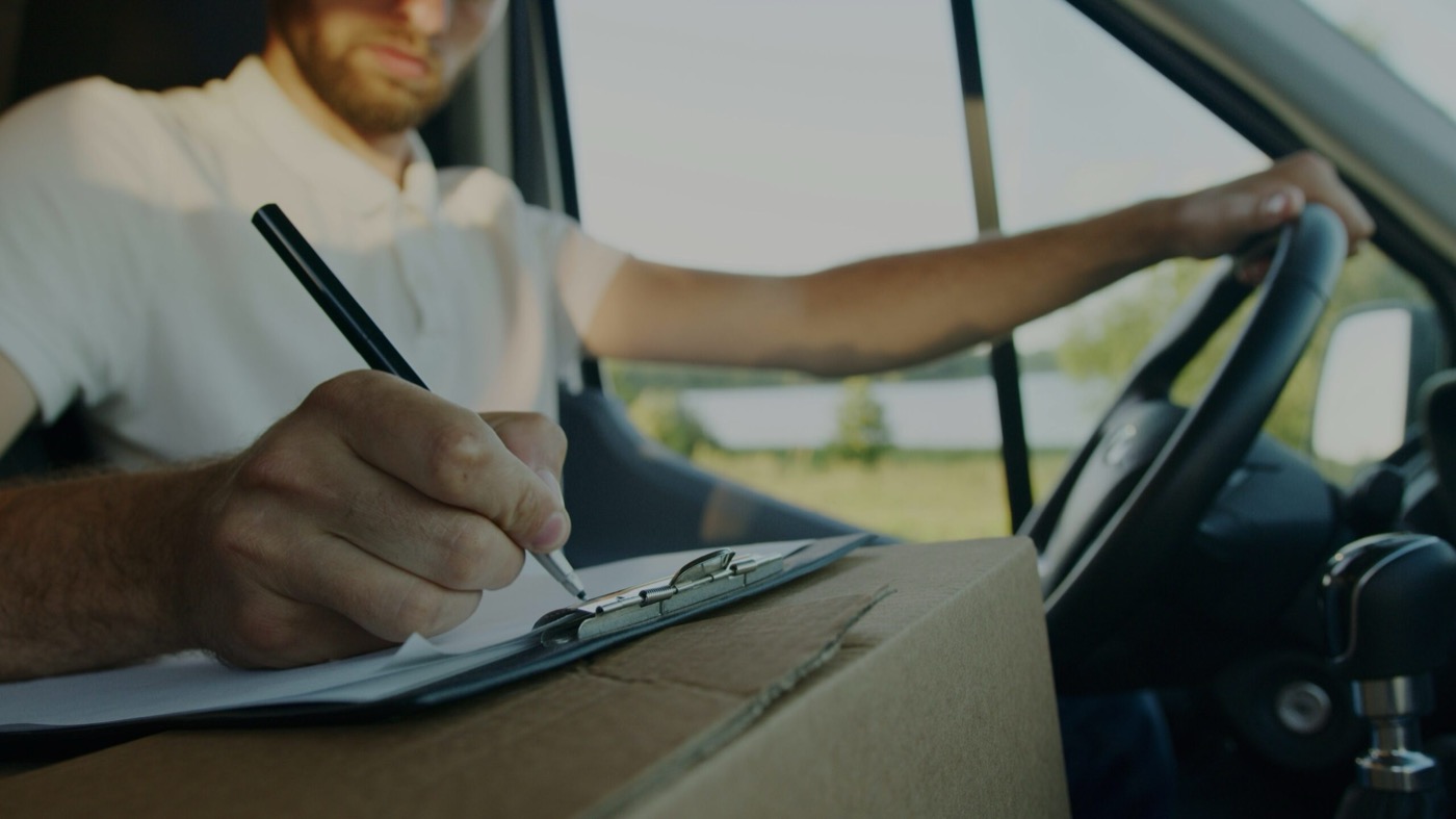 Chauffeur signant un bon de livraison au volant, colis posé sur le tableau de bord
